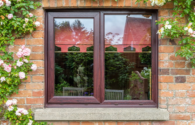 A beautiful double glazed window in rosewood on a brick wall