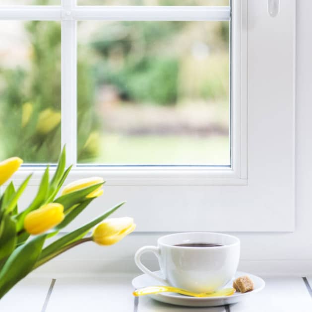 Close up of an Everest white tilt and turn window made from uPVC with a coffee in front of the window