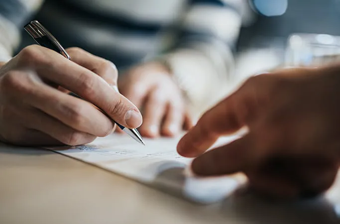 Hands signing a document with a pen