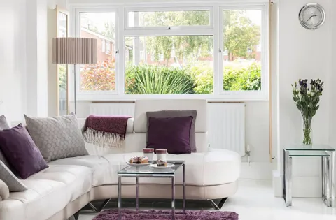White leather sofa with purple pillows and a view of trees outside