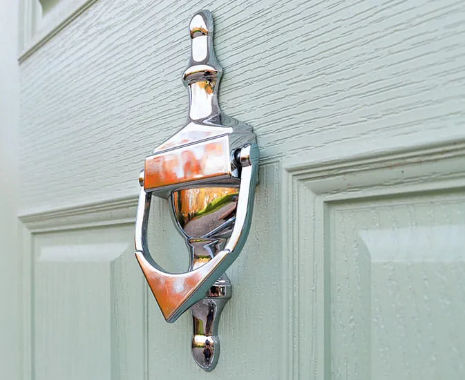 Silver door knocker on a light sage green door