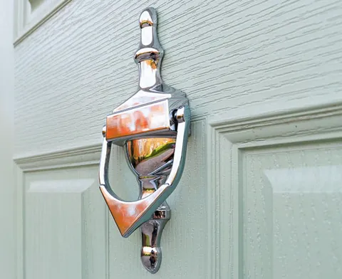 Silver door knocker on a light sage green door