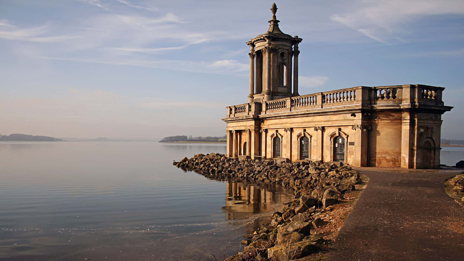 Light stone building by lake reflecting sunlight