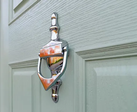 Silver door knocker on light sage green door