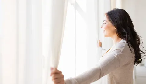 Woman opening white curtains at a window