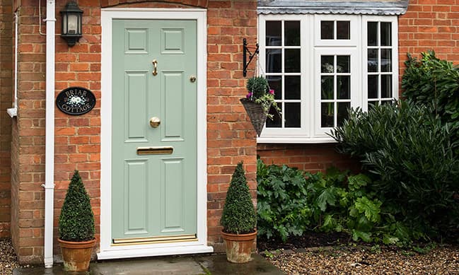 Sage green door with white trim on a brick home