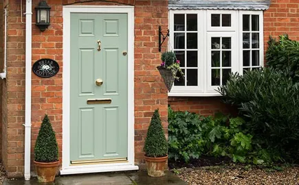 Sage green door with white trim on a brick home