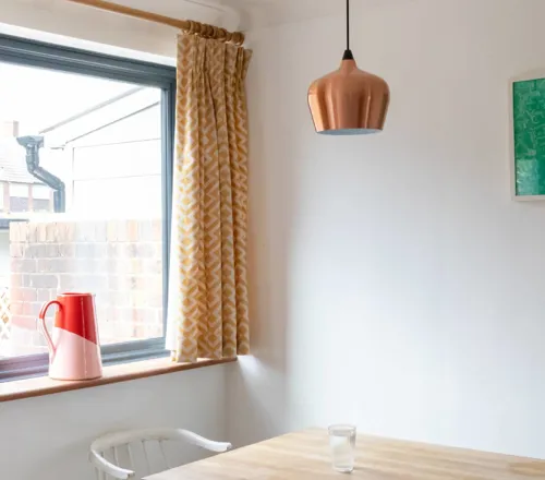 Yellow patterned curtains by window with red pitcher and copper pendant lights