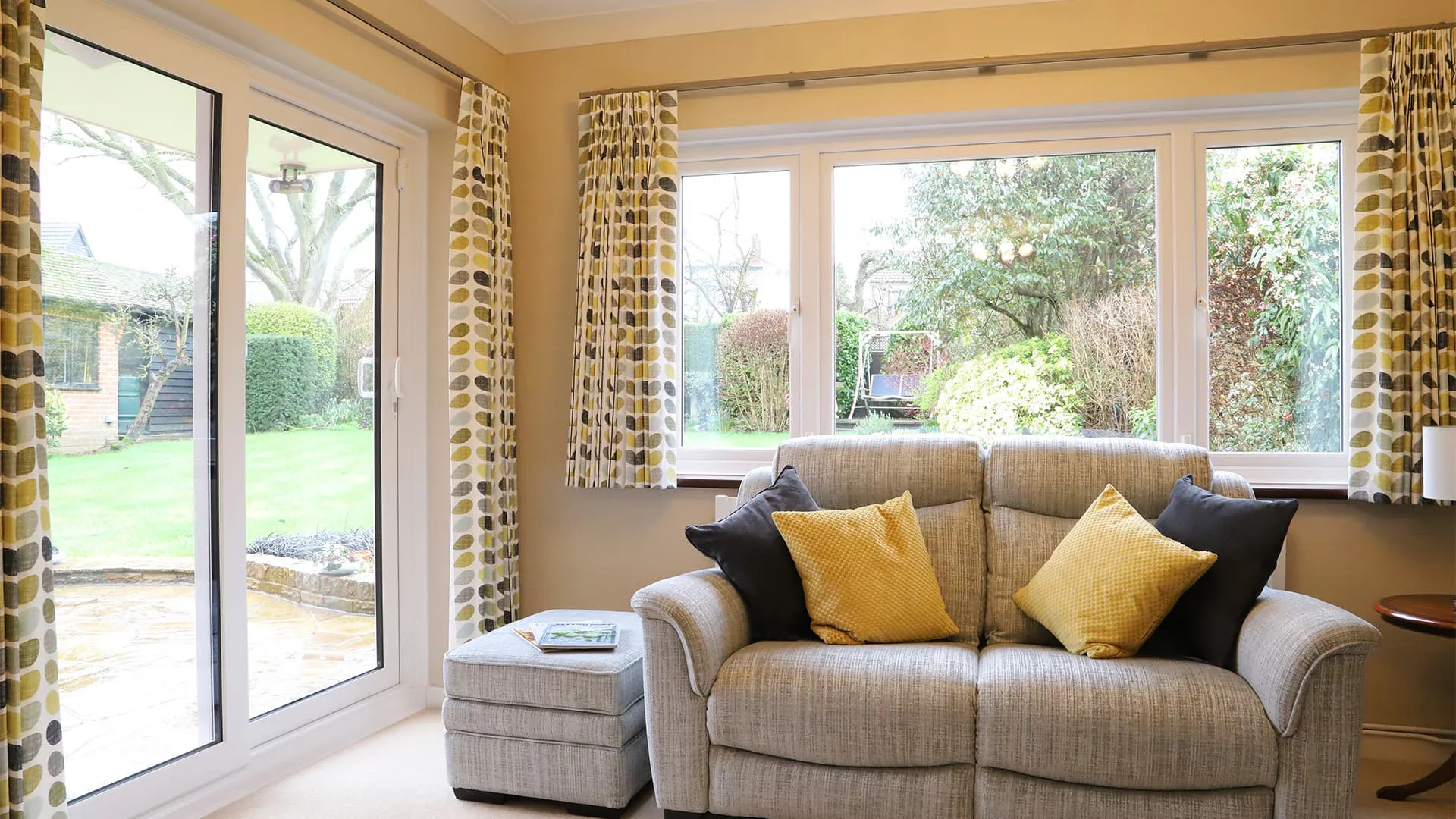 Gray sofa with yellow and black pillows in a room with patterned curtains and a view
