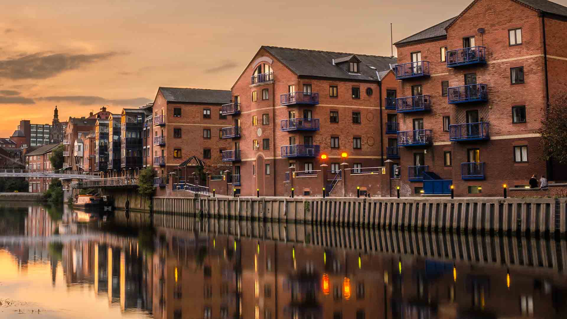 Brick buildings reflecting on calm river water at sunset