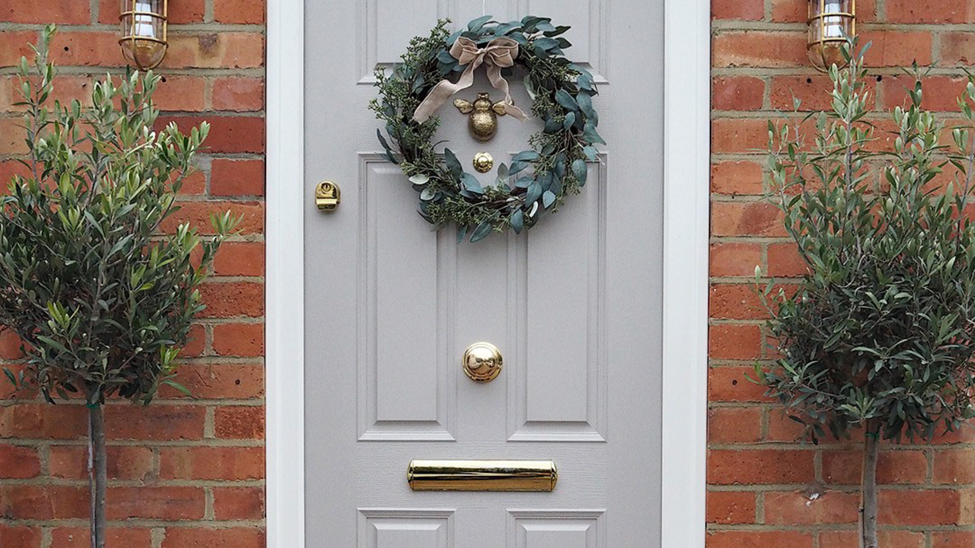 Light gray door with greenery wreath and potted olive trees