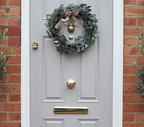 Light gray door with greenery wreath and potted olive trees