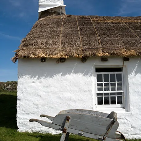 Whitewashed cottage with thatched roof and old wheelbarrow