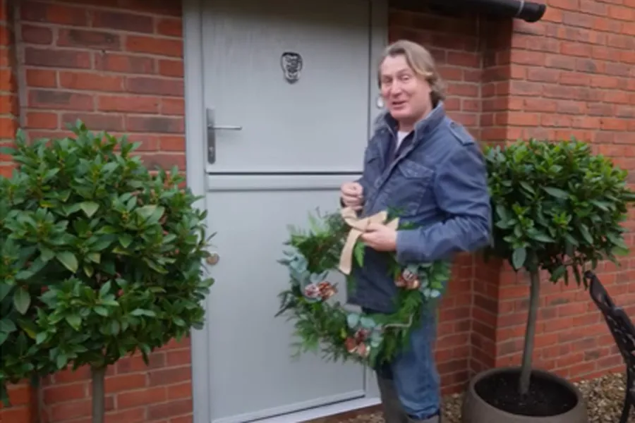 Man holding a festive wreath on a light gray door