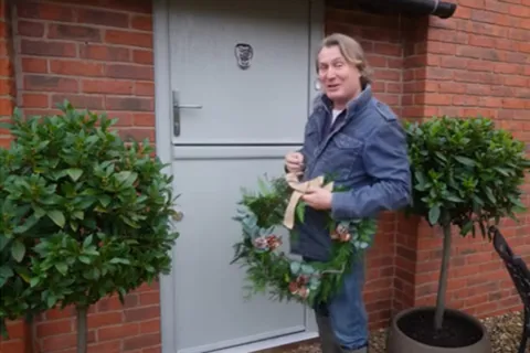 Man holding a festive wreath on a light gray door