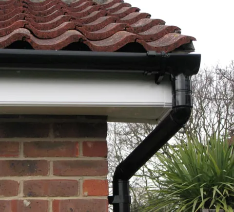 Black gutter corner with white fascia board on red brick wall