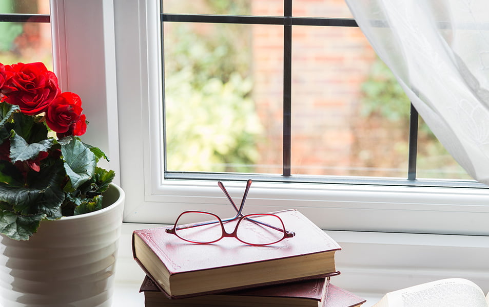 Red eyeglasses on stack of red books by window with flowers