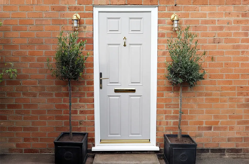 Light grey door with gold accents on brick wall