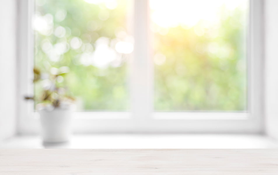 White wooden surface in front of a window with out of focus greenery