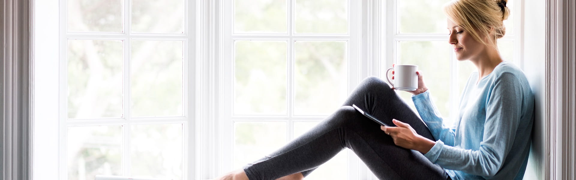 Woman relaxing by window with coffee and tablet