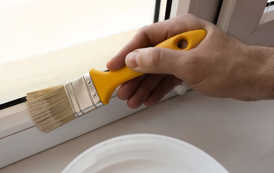 Hand painting window frame with a yellow handled paintbrush