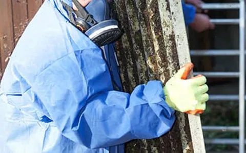 Person in protective gear carrying a weathered corrugated metal sheet