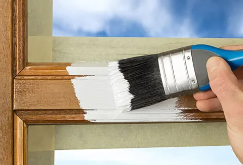 Painting wooden window frame white with a paintbrush