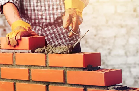Person building a brick wall with mortar